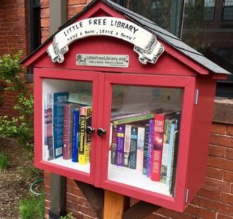 a miniature house-shaped bookshelf on someone's front lawn for sharing books